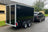 Black Boxxa trailer being towed by a car on a road with a building and trees in the background.