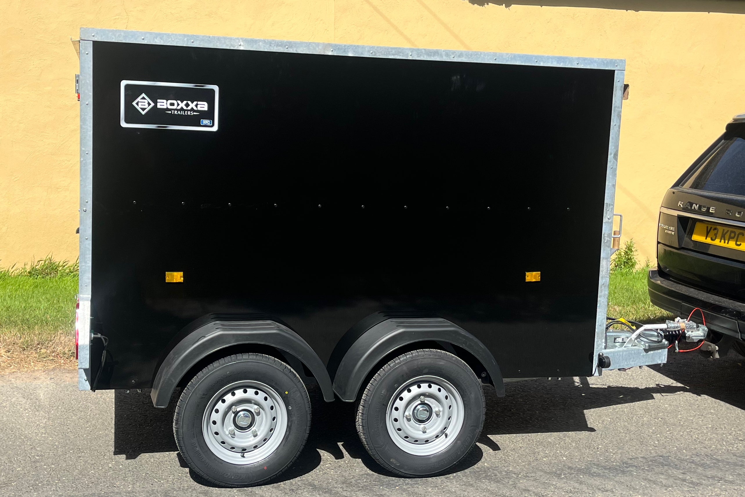 full side view ion a black twin axle Boxxa with 2 of the 4 wheels visible and the boxxa branding on the top left of the trailer body.