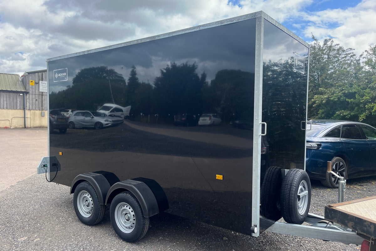 A large black boxxa trailer, side view, with twin axle and front mounted spare wheel.