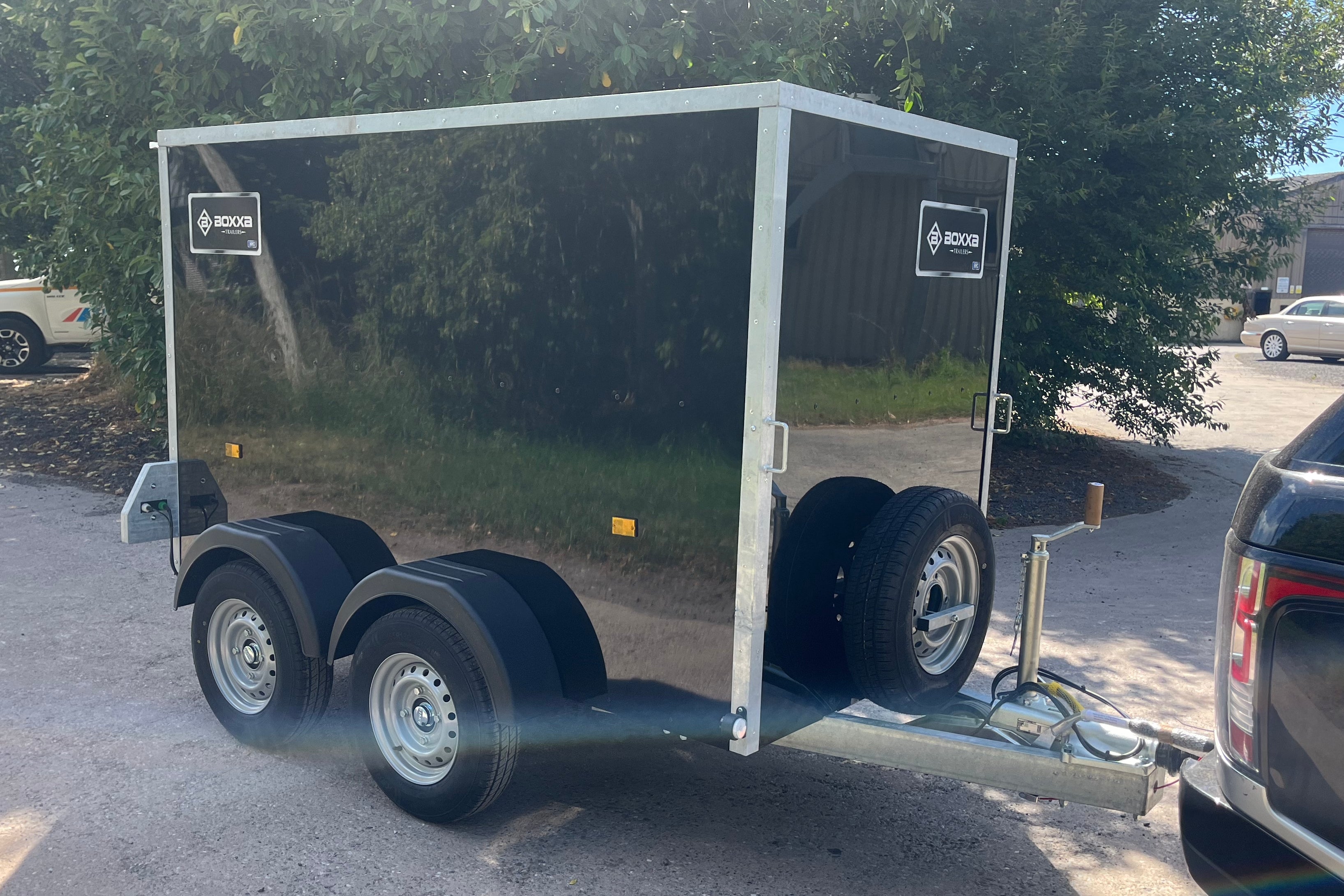 A black boxxa trailer with silver metal trim and dual rear wheels, The trailer has visible' logos on the side panels.