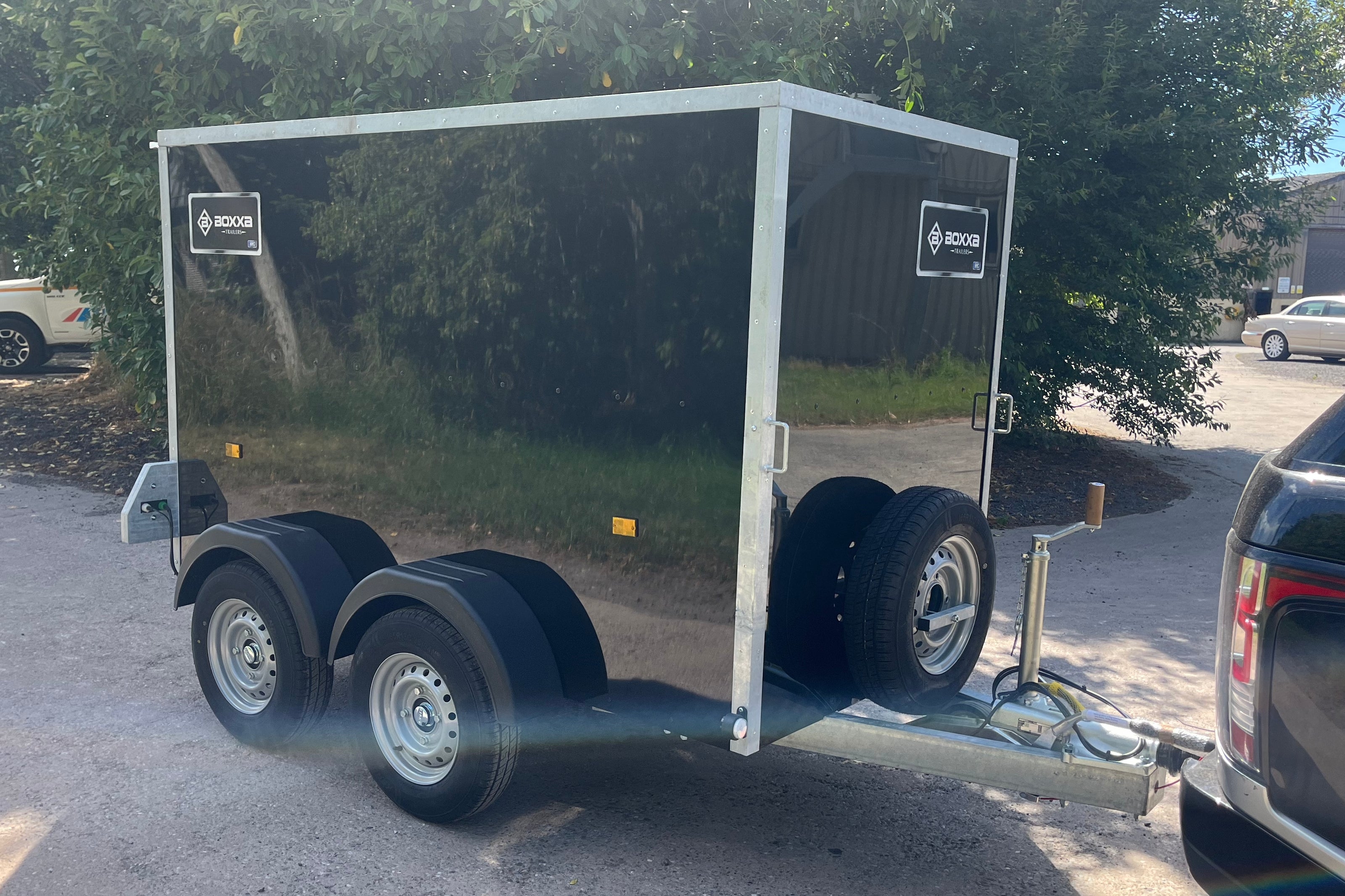 A black boxxa trailer with silver metal trim and dual rear wheels, The trailer has visible' logos on the side panels.