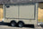 A beige enclosed cargo trailer with silver metal trim and dual wheels, parked outdoors against a tan building wall.