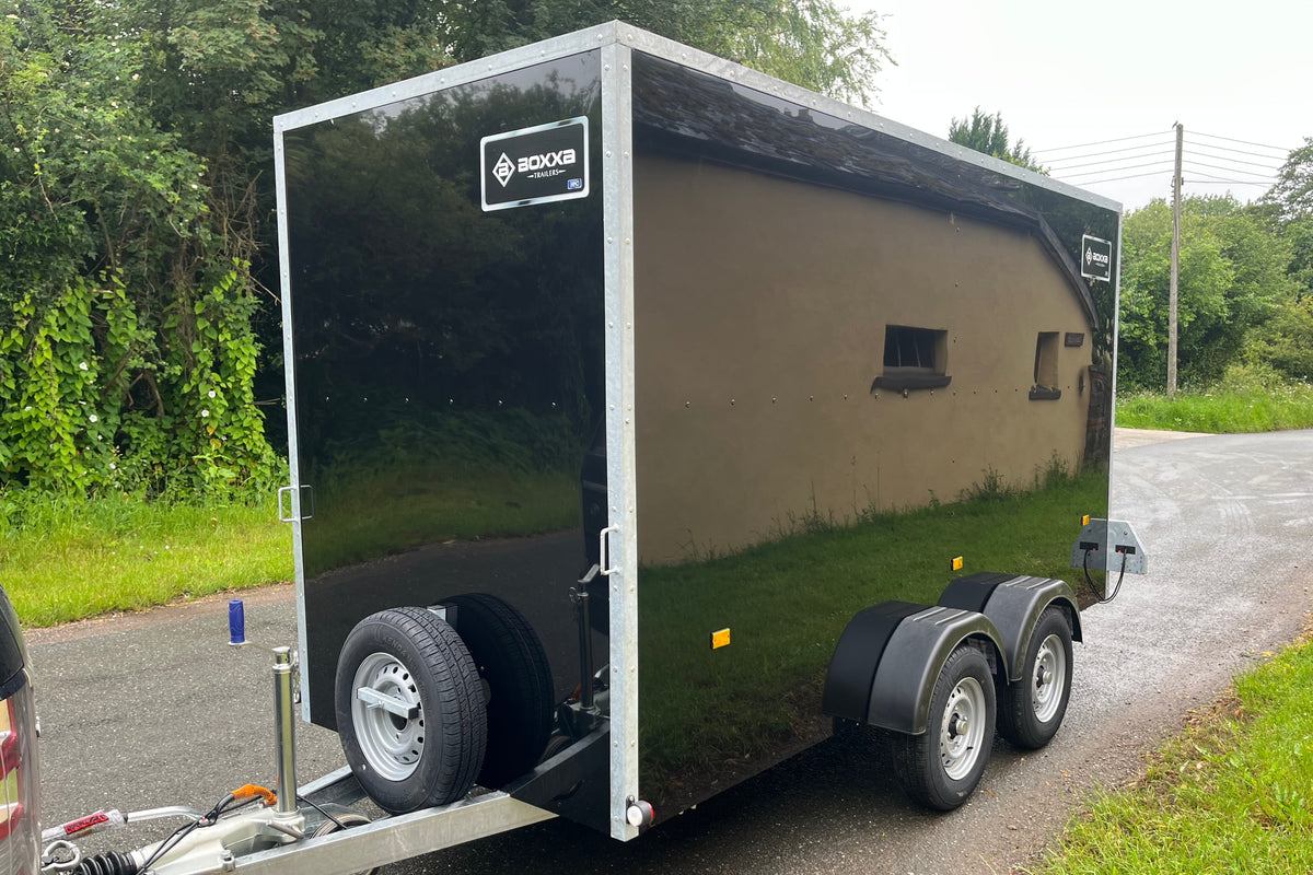 front view of a twin axle black boxxa trailer showing mounted spare wheel and towing gear.