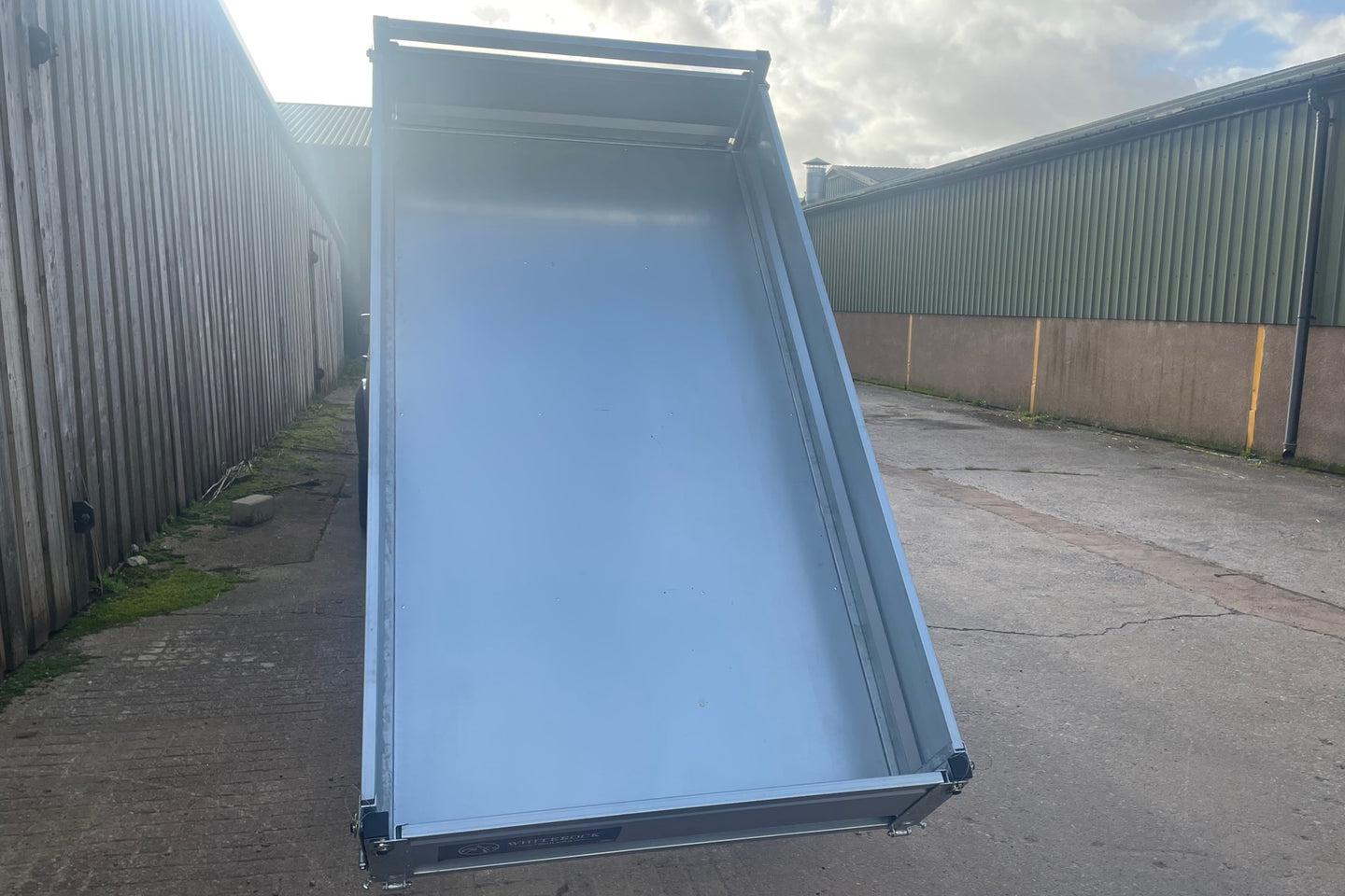 Rear view of a flatbed trailer with sides and steel flooring in full tipping position.